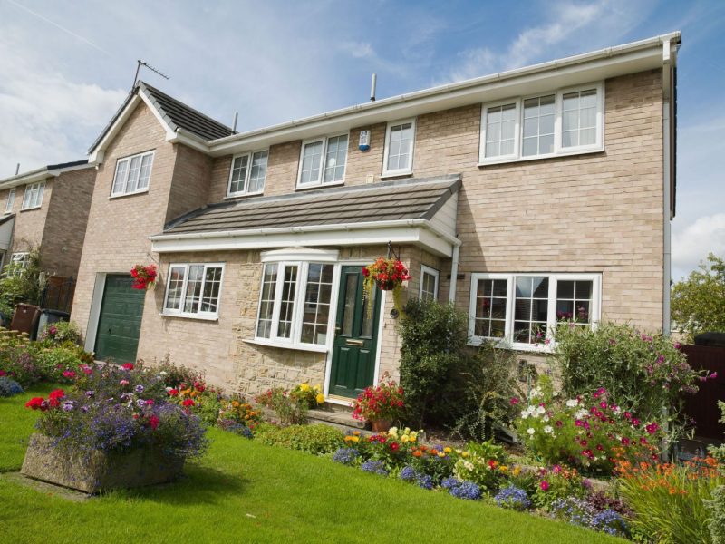 brown brick house with flower filled garden and white casement windows