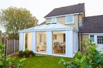 External view of a white conservatory extension with large glass panes and pointed roof