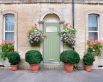 Light green composite door surrounded by sash windows and flowers