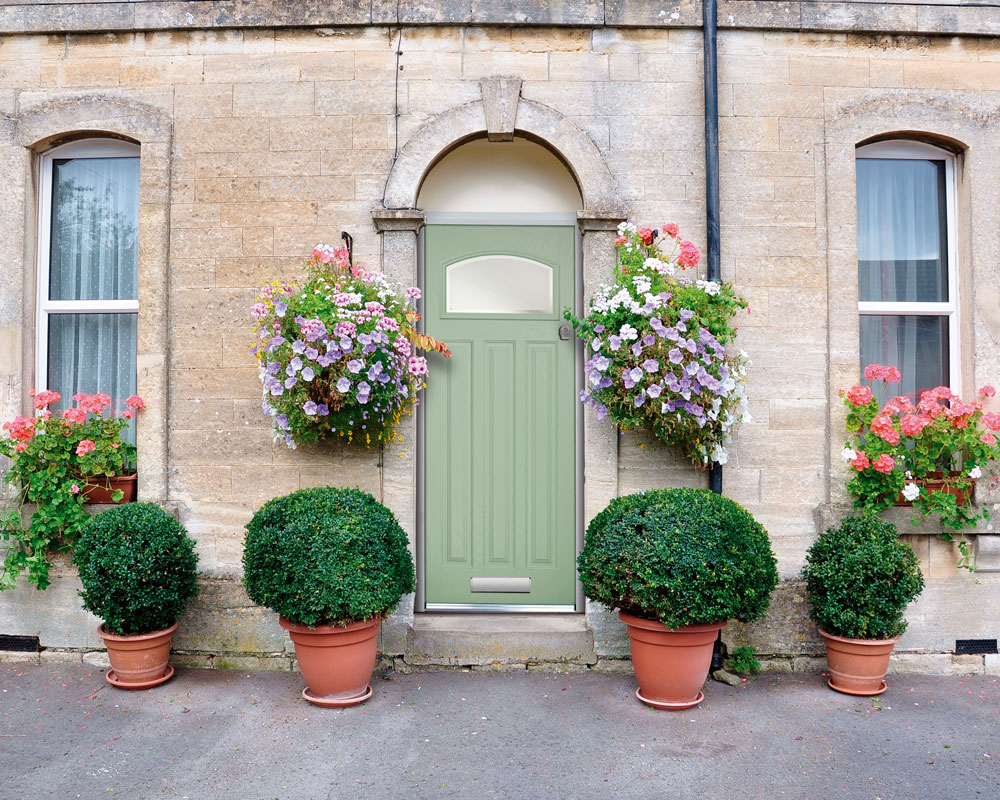 Light green composite door surrounded by sash windows and flowers